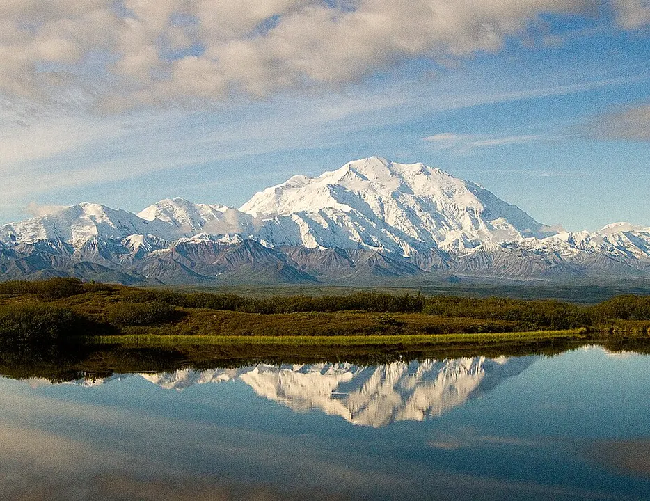 A huge snow-covered mountain rising above a wild green tundra.