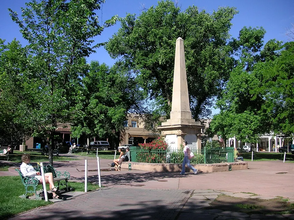 A sunny town square with adobe-style buildings and a long porch.
