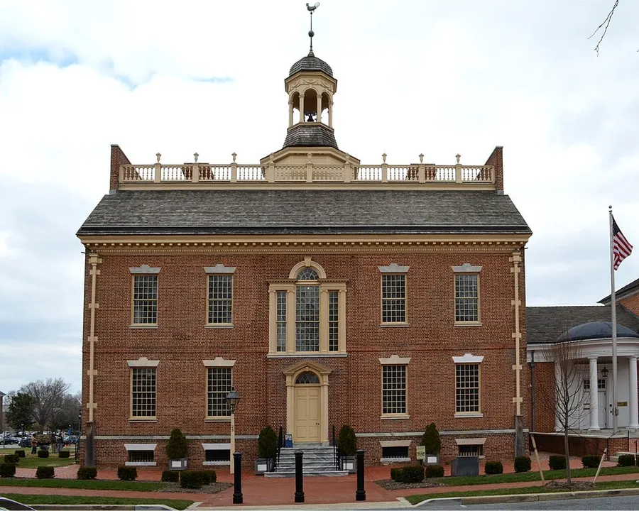 A small red-brick colonial building with a white cupola on a green.