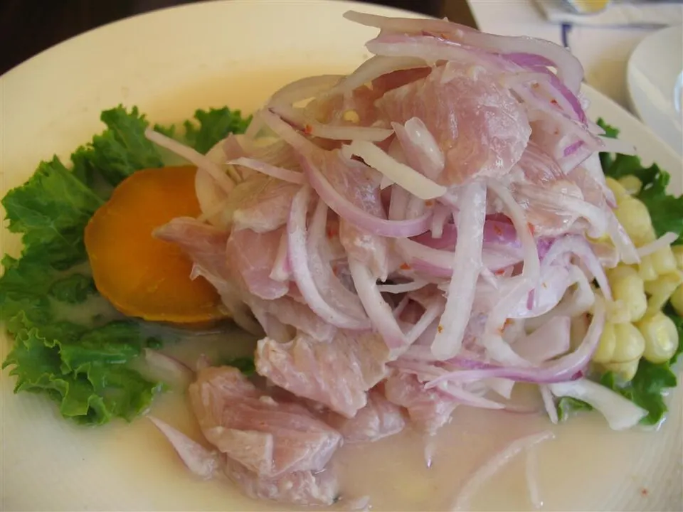 A plate of raw fish pieces with onion, corn and sweet potato.