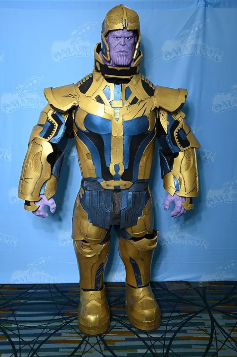 A cosplayer in huge gold and blue armour with a purple-skinned mask, standing in front of a blue backdrop.