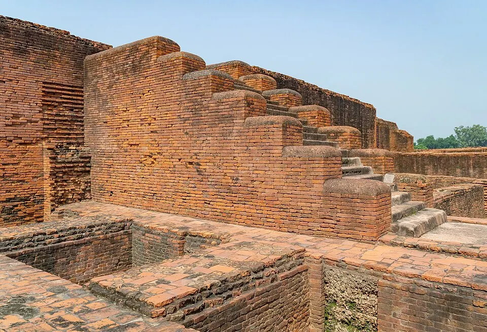 लाल ईंटों से बने एक प्राचीन विहार के खंडहर, जिनमें सीढ़ियाँ और ऊँची दीवारें दिखती हैं।