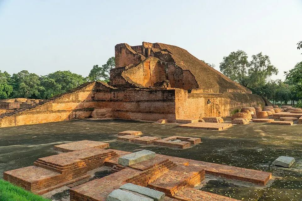 The weathered remains of a huge brick stupa rise behind low brick foundations and small stupa bases.