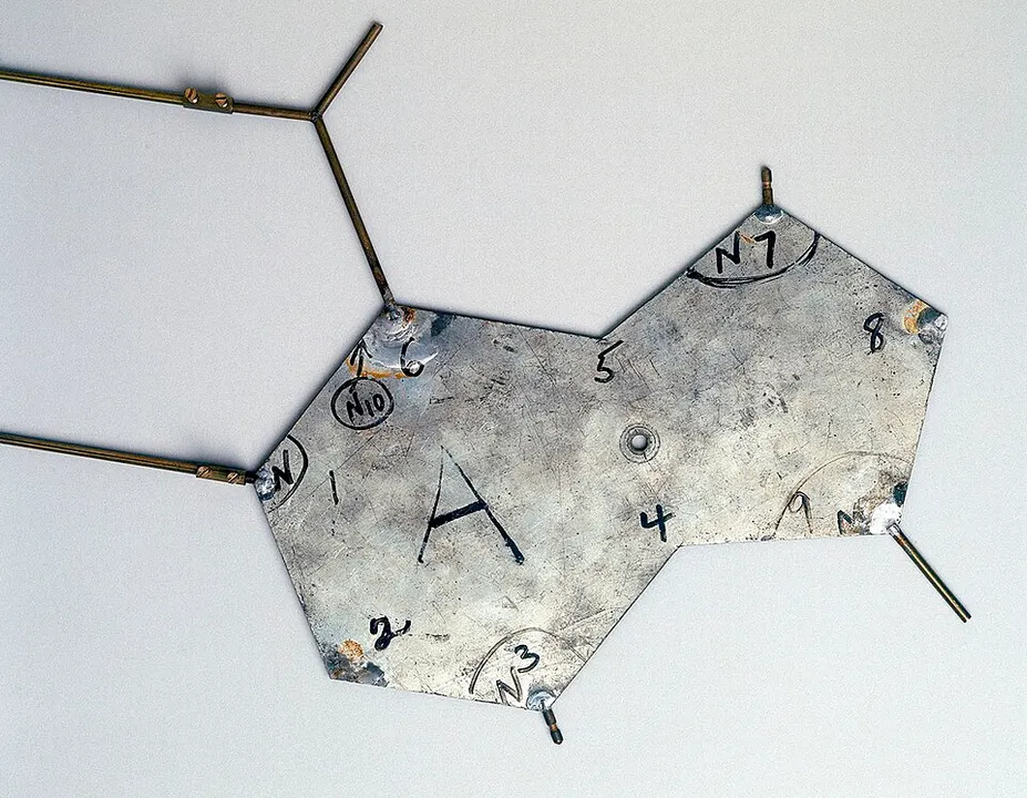 A flat, hexagon-shaped metal plate with brass rods, marked with the letter A and numbers, on a pale background.