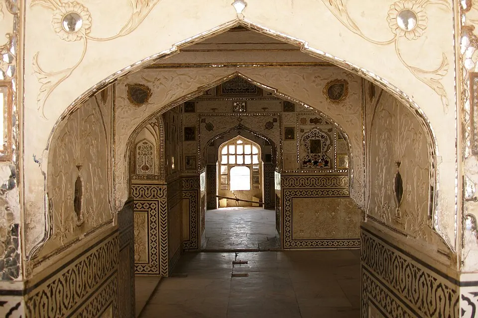 A view through carved arches into a palace hall decorated with inlaid mirror work and painted panels.