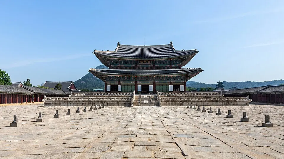 A two-storey traditional Korean palace hall with a dark tiled roof stands behind a wide stone courtyard.
