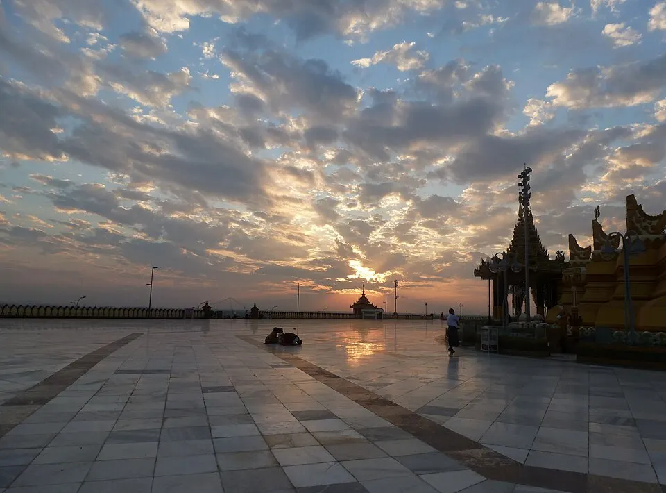 A huge golden pagoda with a tall spire lit at dusk.