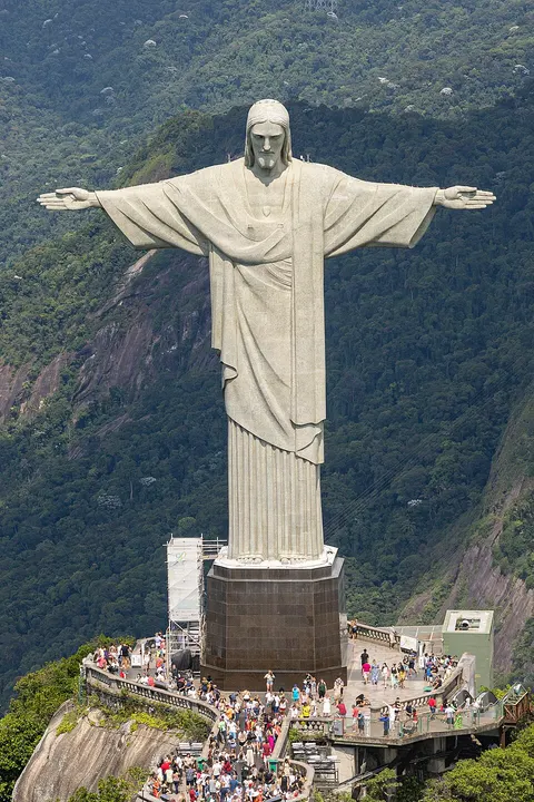 A huge white statue with outstretched arms on a hilltop above a city.
