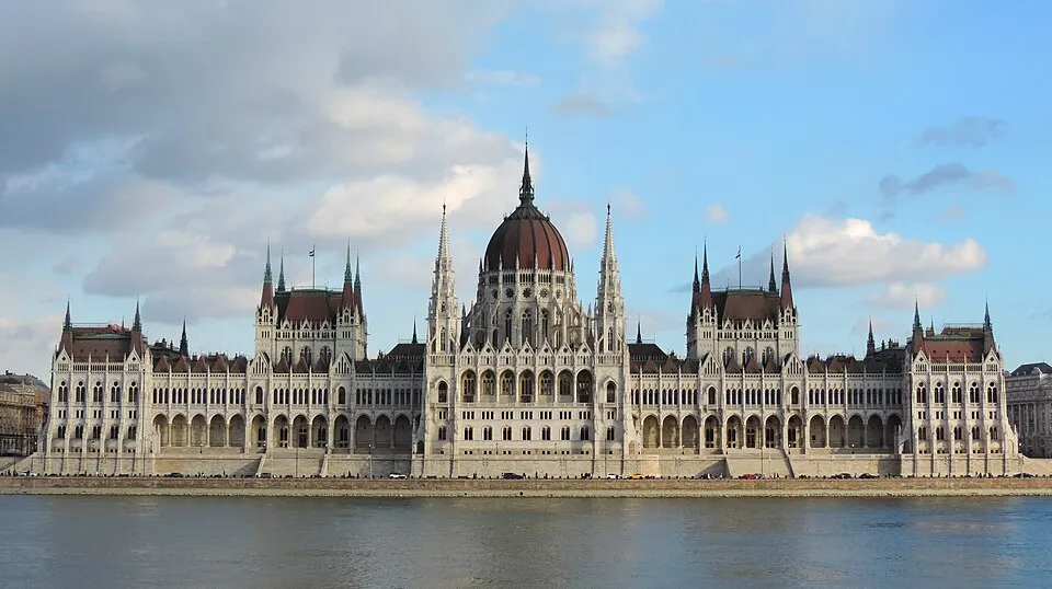 A huge neo-gothic parliament with a central dome on a riverbank.