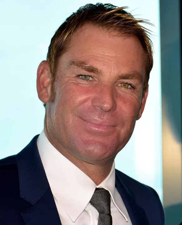 A close-up portrait of a smiling man with spiky blond-tipped hair in a navy suit and white shirt.