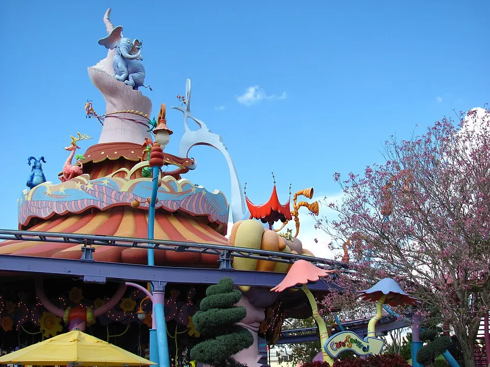 A colourful fairground ride with bright swirly stripes, curved towers and a blue elephant figure on top, against a blue sky.