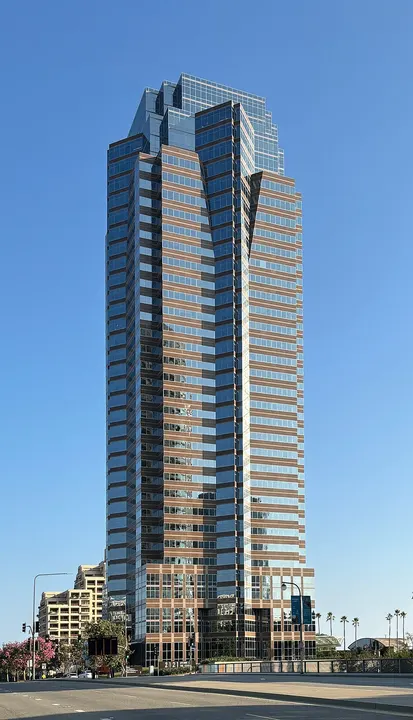 A tall mirrored glass office tower with brown horizontal bands rising against a clear blue sky.