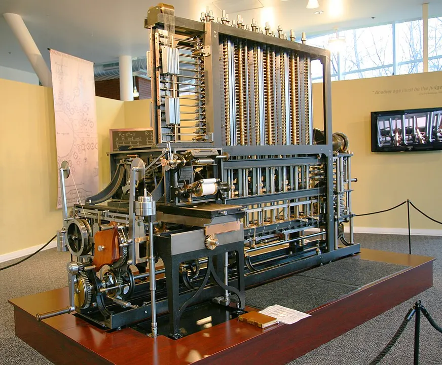 A large brass-and-steel mechanical calculating machine with rows of gears and columns, standing on a wooden platform in a museum.