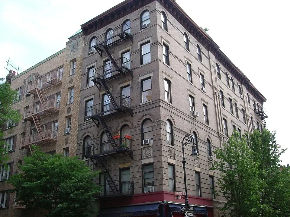 A tall brick apartment building on a street corner with black fire escapes down its front.