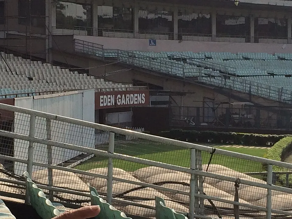 Rows of empty seats at a large cricket ground, seen through a railing, with a sign above a tunnel.