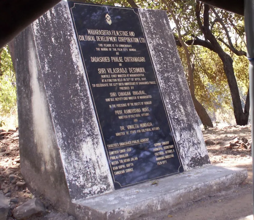 A weathered black stone plaque set on a concrete base among dry trees, its gold lettering carrying a dedication.