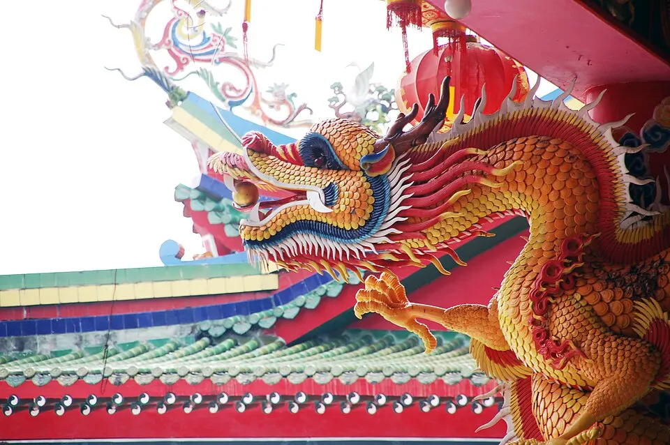 A golden-scaled dragon sculpture with a red mane and curling horns coiled around a red temple roof.