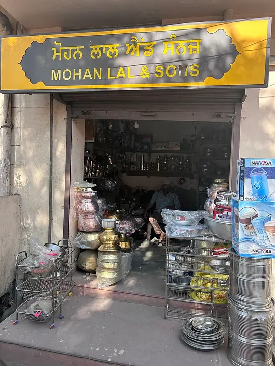 A small shop front stacked with brass pots, steel containers and plates.