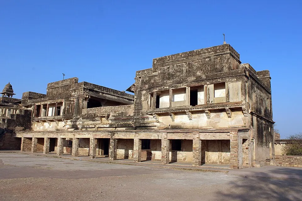 A weathered two-storey stone building with open arches inside an old hilltop fort.
