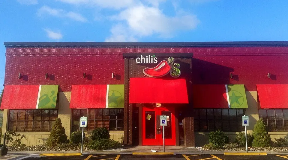A red-brick restaurant with red awnings, a red front door and a lit chili-pepper sign under a blue sky.