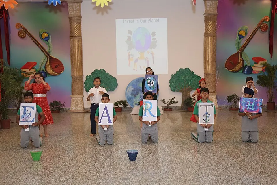Schoolchildren in a decorated hall holding up letters that spell a word, with a planet picture projected behind them.
