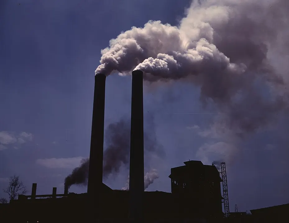 Two tall dark factory chimneys pouring thick smoke into a deep blue sky.