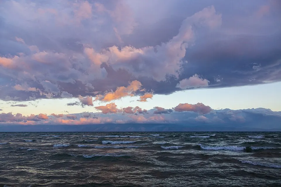 Dark choppy waves on a huge lake under heavy pink and purple clouds at sunset.