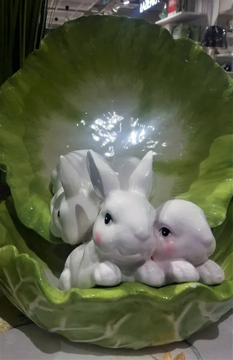 Three white china rabbits with pink cheeks nestled inside a green leaf-shaped dish.