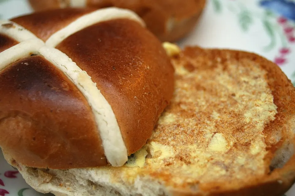 A toasted bun with a white cross on top, spread with melted butter, on a floral plate.