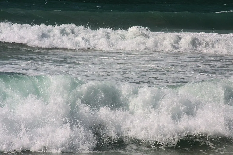 Large white-capped waves rolling and breaking on a dark teal sea.