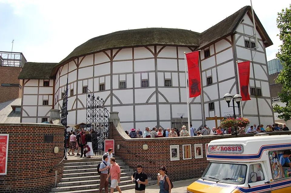 A round white timber-framed theatre with a thatched roof, with crowds on the steps in front.