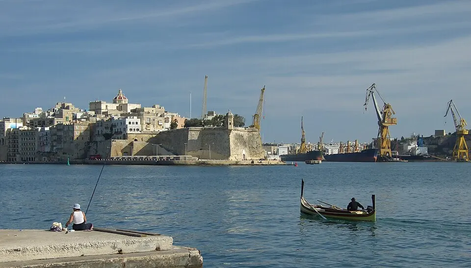 Honey-coloured fortified walls and domes rising above a harbour.