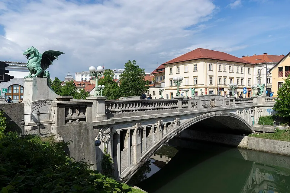 A stone bridge guarded by green dragon statues over a small river.
