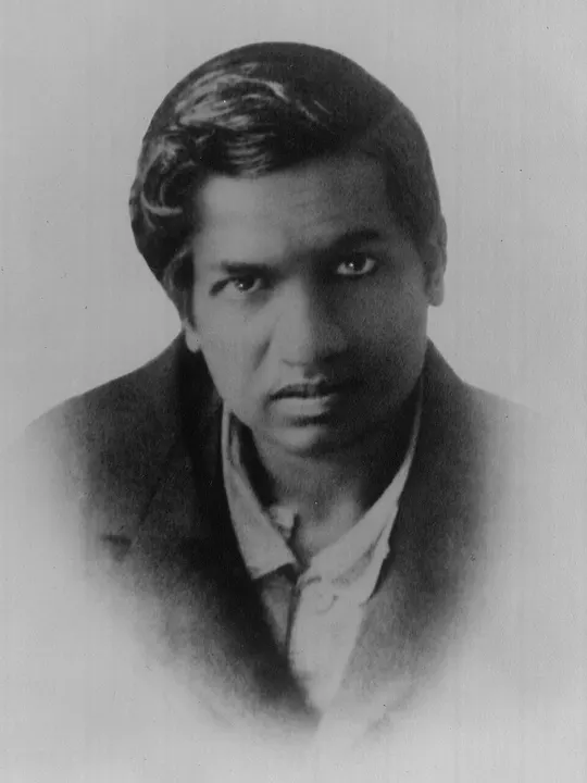 A formal portrait of a young man in a white shirt and dark cap.