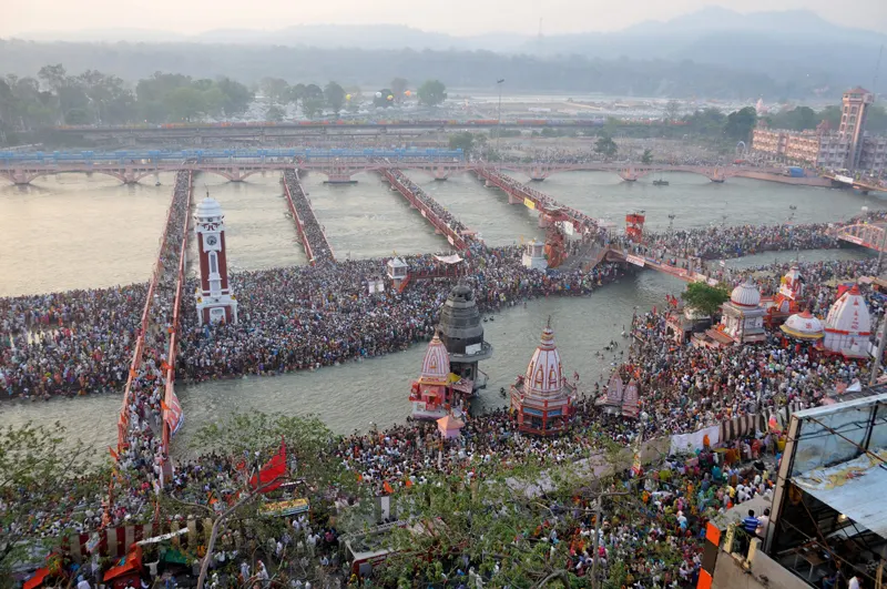A vast crowd of pilgrims bathing at a river bank under a hazy sky.