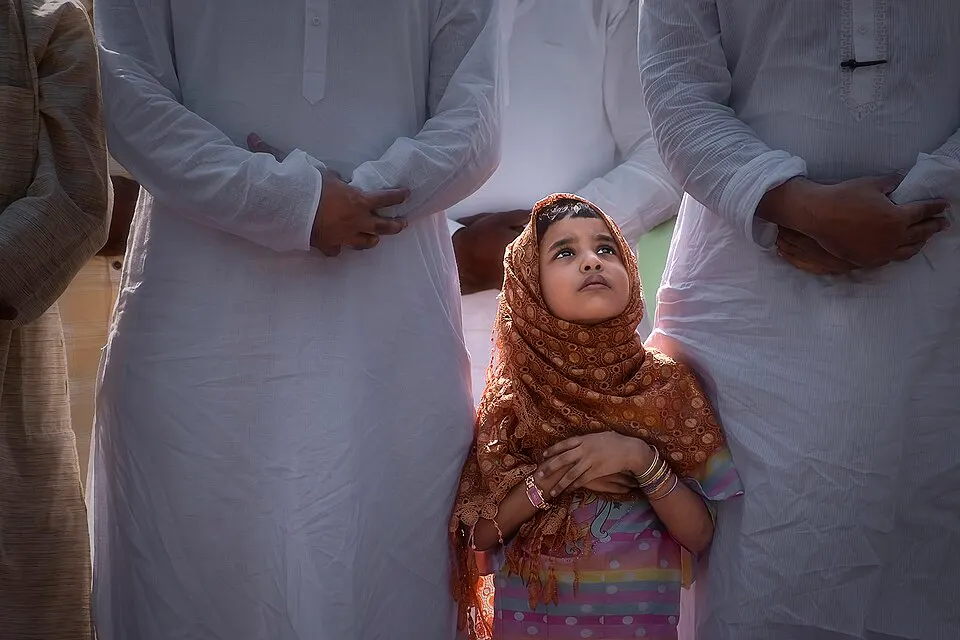 A young girl in a headscarf standing among worshippers at Eid prayers.