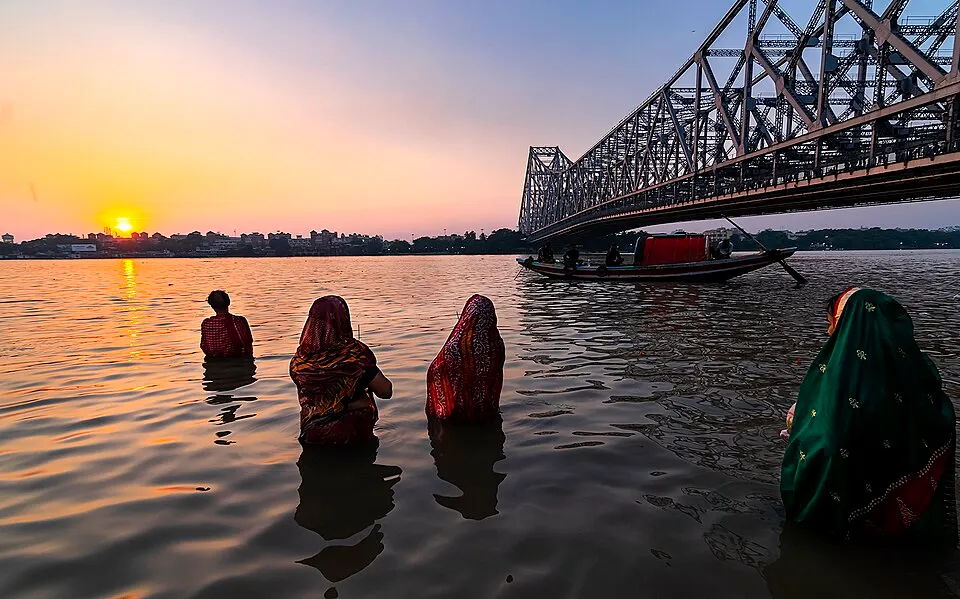 Devotees standing waist-deep in water at dusk, offering prayers.