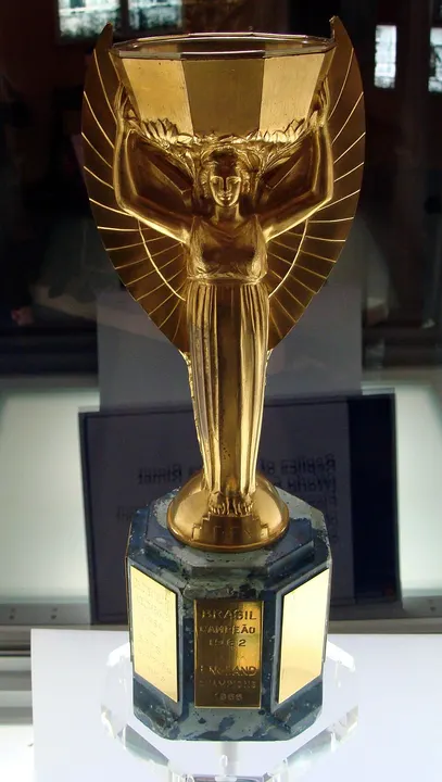 A golden winged figure holding up a bowl on a dark stone base with gold plates, in a museum case.
