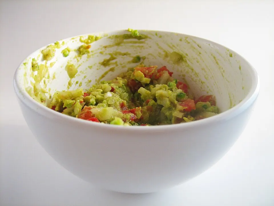 A bowl of chunky green dip with tortilla chips beside it.