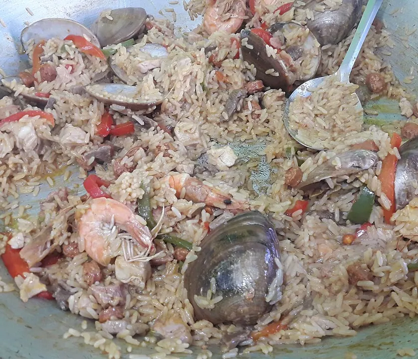 A wide shallow pan of saffron rice with meat and vegetables.