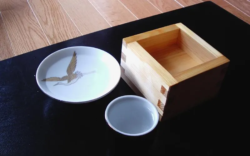 A small ceramic cup and a wooden box of clear drink on a table.