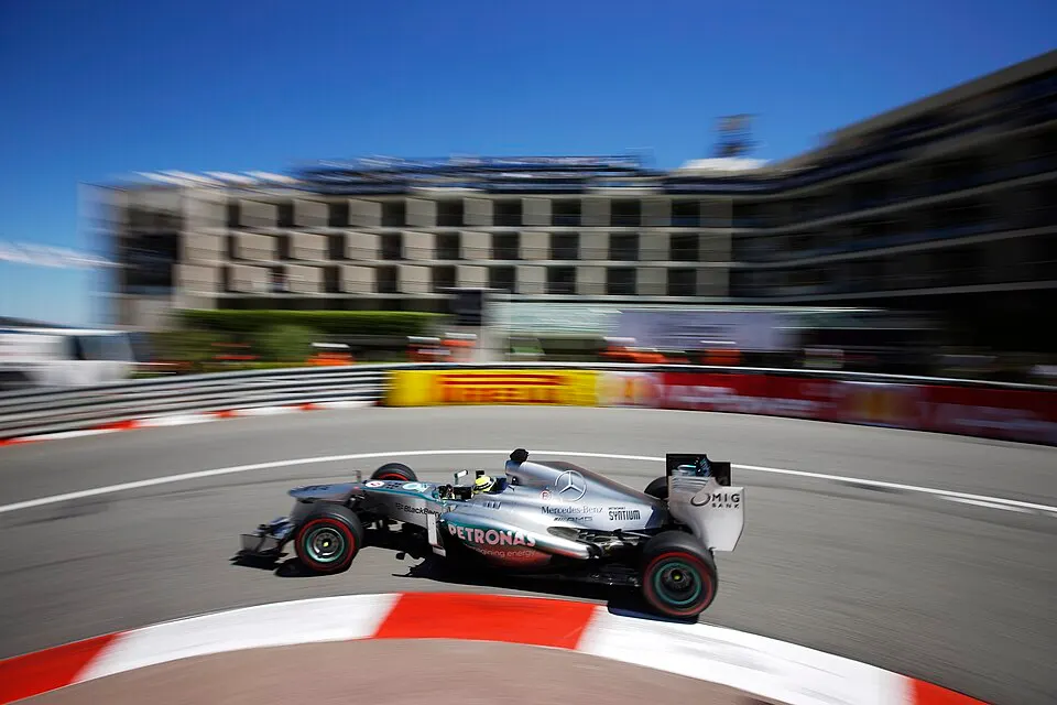 Racing cars on a narrow street circuit beside a harbour.