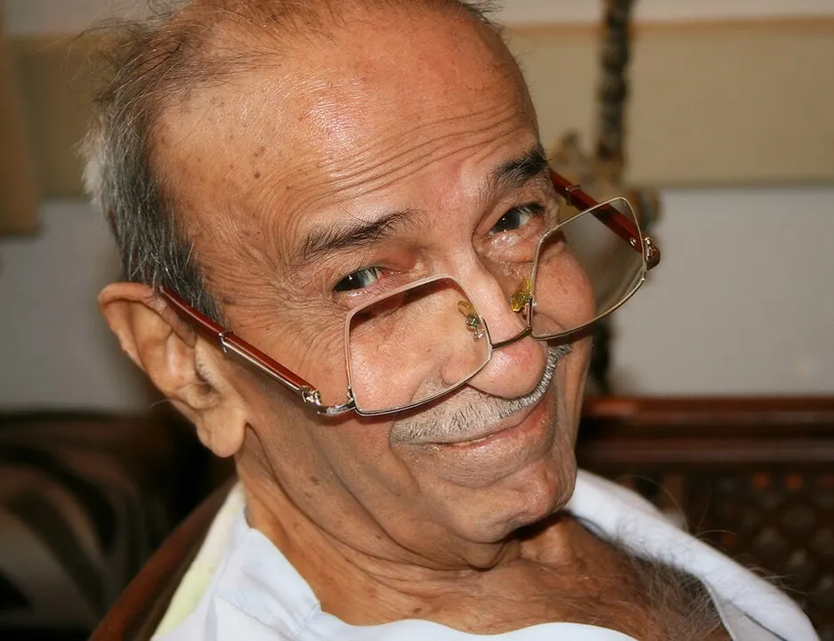 Close-up of a smiling elderly man peering over the top of his glasses, which sit low on his nose.