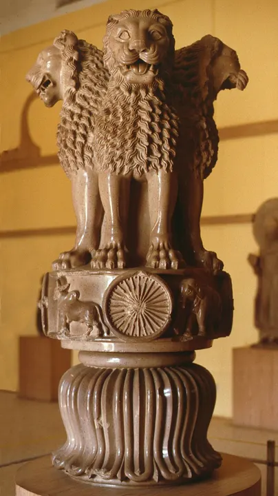 A polished sandstone sculpture of four lions standing back to back on a round base carved with a wheel, an elephant and a bull, above an upside-down lotus.
