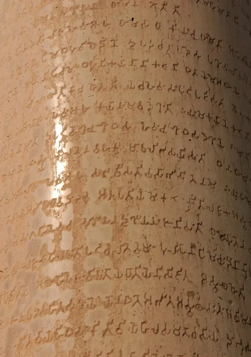 A close-up of a smooth stone pillar surface covered in rows of ancient carved letters.