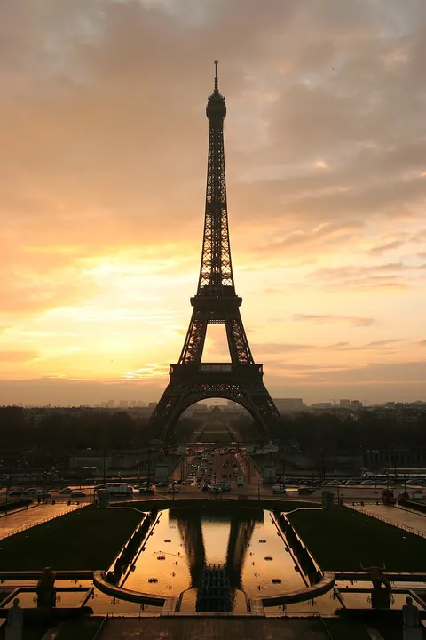 A tall lattice tower silhouetted against an orange sunrise sky above a city.