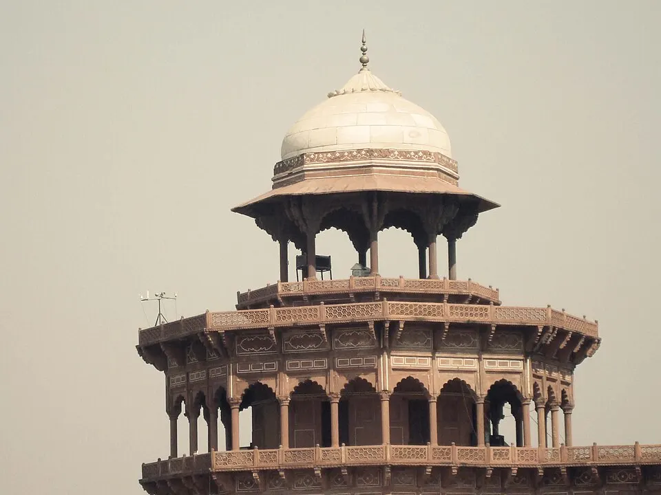 A white marble dome on top of a red sandstone tower with arched openings.