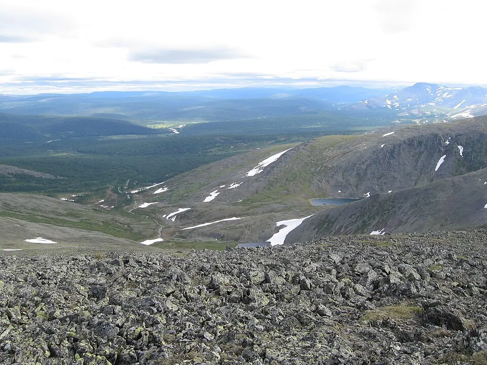 A rocky mountain ridge with patches of snow looking out over a wide forested valley.