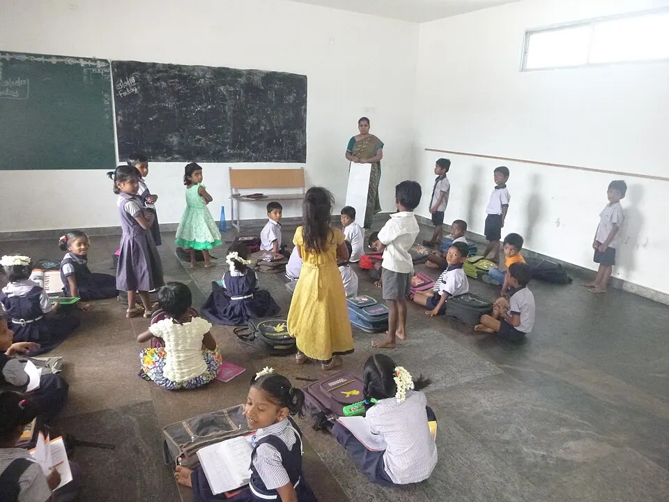 Young schoolchildren in uniforms sitting and standing in a classroom with a teacher near the blackboard.