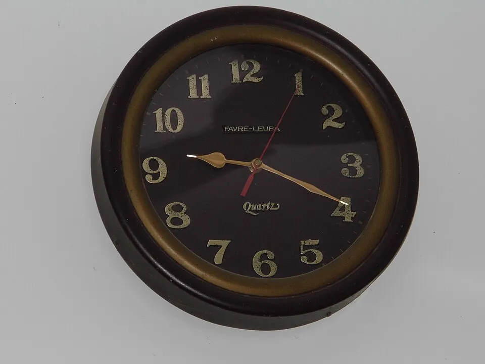 A round wall clock with gold numbers, an hour hand, a minute hand and a red second hand.